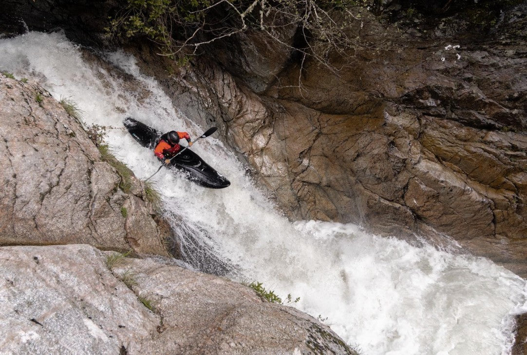 Canoiest paddling in a black boat down white water between rocks